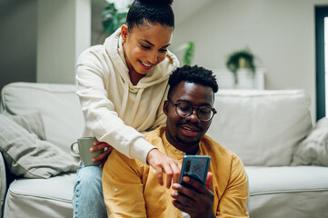 Multiracial couple at home while drinking coffee and using smartphone