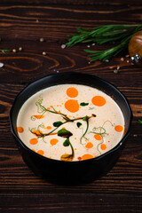Fresh champignon cream soup in a bowl served with green peas and oil on a wooden table.