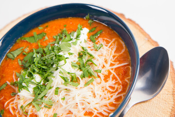 Italian tomato soup served with cream, mozzarella cheese and fresh parsley in a bowl, on a wooden  pad on a white backround