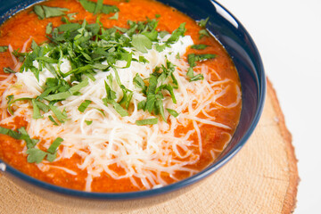 Italian tomato soup served with cream, mozzarella cheese and fresh parsley in a bowl, on a wooden  pad on a white backround