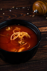 Fresh tomato soup with fried onion rings in a bowl on a wooden table.