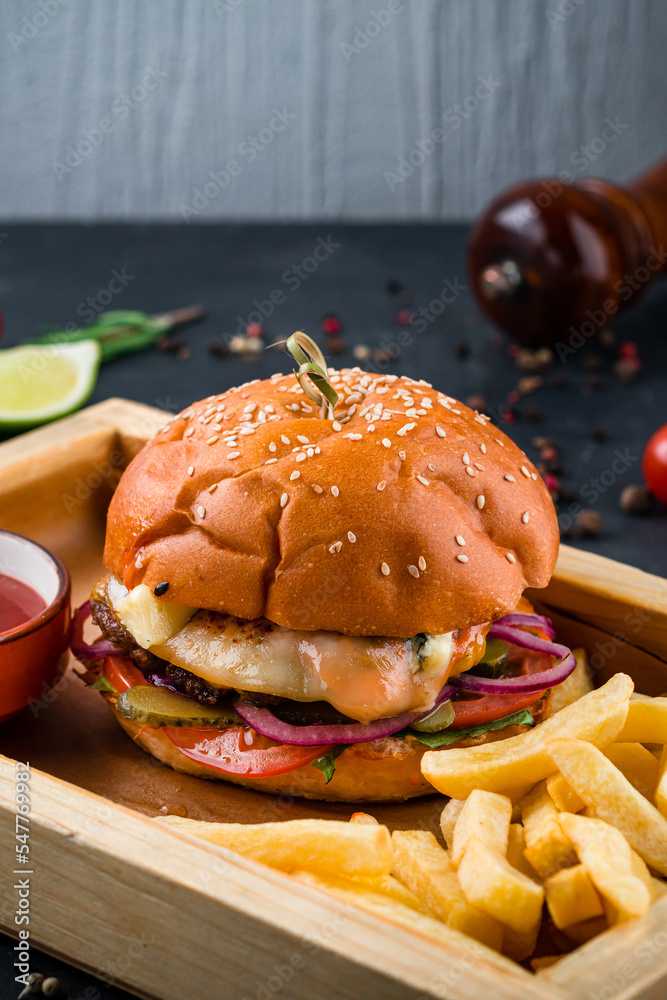 Sticker American style beef burger with tomato, fried eggs, pickle, onion, lettuce, cheese sauce on a wooden board with french fries and ketchup.