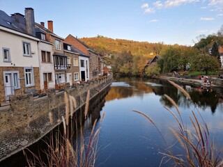 Fototapeta na wymiar Riverbank of picturesque village of La Roche En Ardenne (Belgian Ardennes) along the river Ourthe at golden hour (sunset) with reflection of stone houses in the water