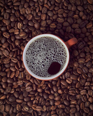 Black coffee in a small cup with a background of roasted coffee beans from Colombia