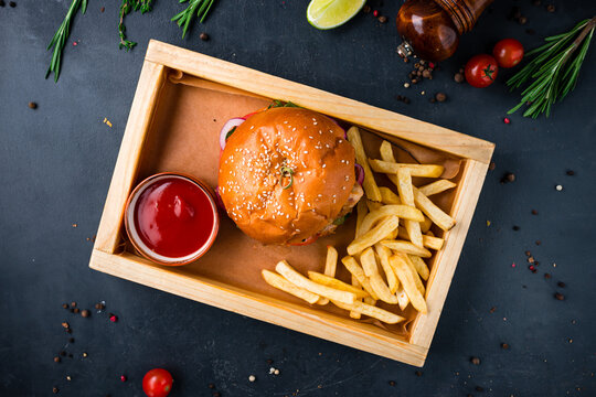 Burger with chicken, tomato, pickle, onion, lettuce, cheese sauce on a wooden board with french fries and ketchup.