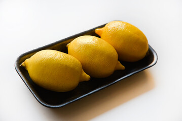 Ripe yellow lemons on a black plastic backing. Delicious lemons from the store on a white background. Yellow lemons packed in a container.