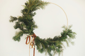 Modern Christmas wreath with velvet ribbon and golden bells hanging on white wall background close...