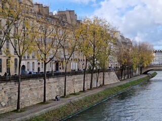Bank of Ile de St Louis on the Seine in Paris, with couple romantically sitting on a bench and golden autumn leaf color