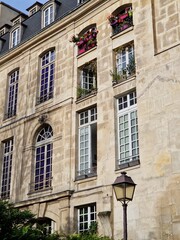 Fototapeta na wymiar Typical Paris facade of old stone building with high windows, flowers and a lantern on sunny day in France