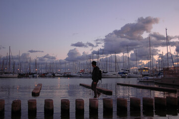 Young stylish man with hat walks on wooden poles at palma de mallorca harbour in sunset