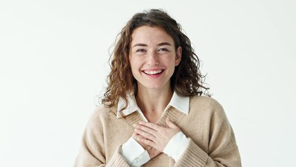 Happy grateful pleased young pretty smiling woman putting hands on chest expressing sincere gratitude, warm appreciation, thanking or feeling touched standing at white background.