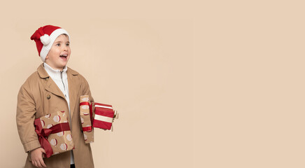 Funny little boy with Christmas gifts and shocked face on light brown background.