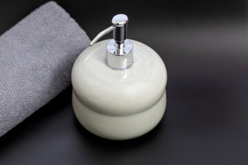Ceramic soap dispenser and folded towel on white marble background.