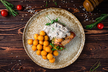 Lunch chicken thigh with mushroom sauce and croquettes, fried mashed potato balls with tomatoes and greens on a plate.