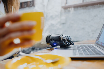 woman with bionic hands is working on a laptop and drinking coffee in a coffee shop technology in...