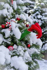 Outdoor decorated Christmas tree covered in snow.  The ornaments are bright red and there are elf legs sticking out from the tree.