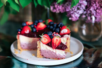 Cheesecake with strawberries and blueberries, close-up, in a rakoze, against a background of lilacs.