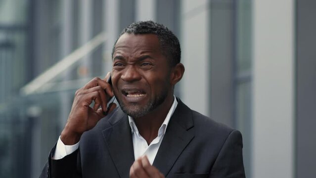 Business problems. Irritated middle aged black man ceo talking on phone with employee, scolding about mistakes outdoor