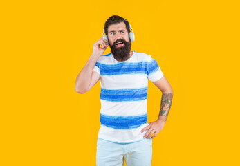 curious hipster man listen music in earphones isolated on yellow background. man in earphones