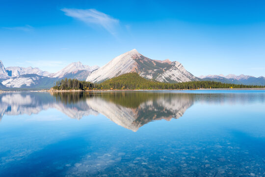 Mountain landscape at the day time. Lake and forest in a mountain valley. Natural landscape with a blue sky. Reflections on the surface of the lake. Banff National Park, Alberta, Canada.