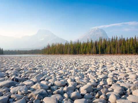Mountain landscape at the morning. River coast with stones and forest in a mountain valley. Natural landscape with a blue sky and sunshine. Wallpaper. Alberta, Canada.