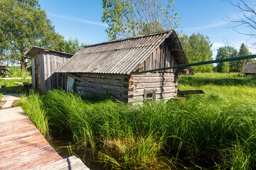 Fototapeta na wymiar an old log Pomeranian bathhouse installed next to a lake overgrown with reeds and grass. Russian North.