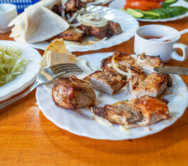 sliced kebab on a plate with onions, cucumbers and sauce. wooden table.