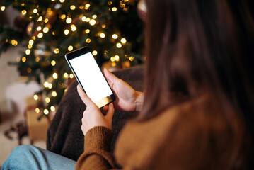 christmas mockup with space for text. christmas advertising, app template. hands holding phone with empty screen on background of golden beautiful christmas tree with lights in evening