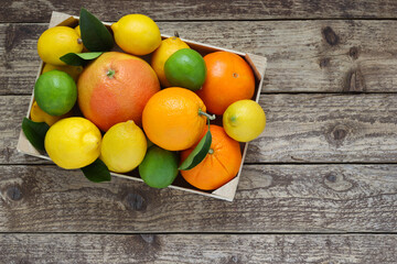 Mix of citrus fruits. Oranges, grapefruit, lemons and limes with leaves in box on wooden background. Top view. Photo from above. - Powered by Adobe