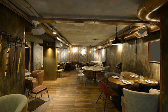 Dining room of a restaurant with dark walls, round wooden tables and vintage chairs and armchairs