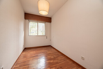 Empty living room with reddish parquet flooring with matching skirting boards and wooden doors with aluminum barred windows