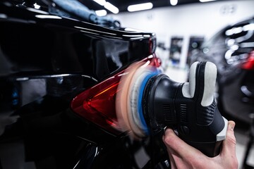 Employee of a car detailing studio polishes the paint of a car with an electric polishing machine