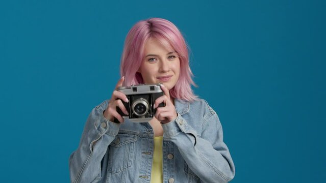 Portrait of cheerful beautiful student female with Pink Color Hairstyle in good mood with analogue camera in studio. Happy pretty young hipster woman tourist taking photo. Photographer taking pictures