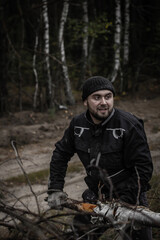 A man with a beard pulls a tree trunk with branches from a pile of fallen trees. A man in work clothes sorts a blockage of trees. The concept of a strong man.