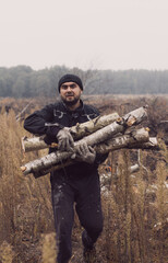 A man carries a pile in two hands. Front view, looking at the camera. A Caucasian man has cut logs for firewood and carries them to the trailer of the car.