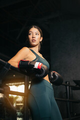 A young Asian woman posing in a boxing ring, the girl is leaning on her back on the ropes. Youth boxing concept.