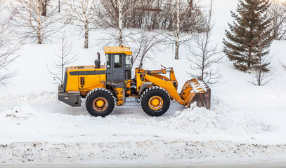 Snow clearing. Tractor clears the way after heavy snowfall. A large orange tractor removes snow from the road and clears the sidewalk. Cleaning roads in the city from snow in winter.