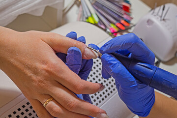 Manicurist master removing cuticles. Processing of rough cuticles and lateral folds of nails on hands with a conical instrument. Medical hardware manicure in a beauty salon