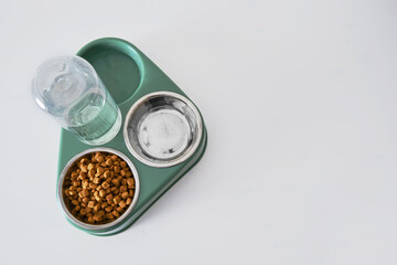 A bowl of dry cat food on a white background . Green triple plate with water for a pet, close-up