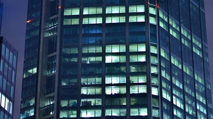 Modern office building in city at the night. View on illuminated offices of a corporate building. Blinking light in window of the multi-storey building of glass and steel. Long exposure at night