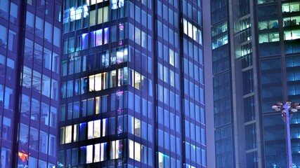 Obraz premium Modern office building in city at the night. View on illuminated offices of a corporate building. Blinking light in window of the multi-storey building of glass and steel. Long exposure at night