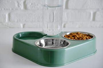 A bowl of dry cat food on the background of a white brick wall. Green triple plate with water for a pet, close-up