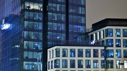 Obraz premium Modern office building in city at the night. View on illuminated offices of a corporate building. Blinking light in window of the multi-storey building of glass and steel. Long exposure at night