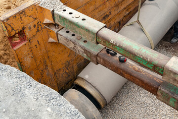 Builder installing big diameter concrete drainage pipe protected by trench support system during...