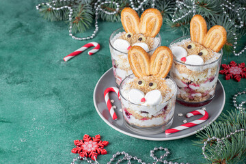 New Year's dessert in glasses the form of cute rabbits with cherries, cookies and curd cream on green background. Symbol of the new year 2023, Copy space