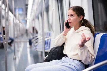 Active girl riding a subway train discusses topical issues on her mobile phone