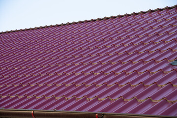 a fragment of a roof with red metal tiles with an attic window, construction