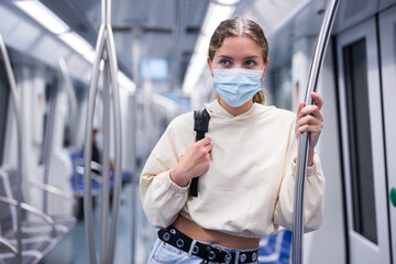 Fototapeta na wymiar Portrait of a young stylish woman in a face mask riding in a subway wagon