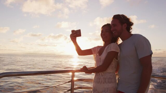 Phone use on cruise ship travel. Smart phone selfie - Romantic couple taking phone selfie by sunset over the ocean on small cruise ship sailing on open sea on vacation
