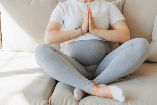 Beautiful young pregnant woman practicing yoga at home on sofa, background light kitchen. Concept meditating health pregnancy